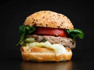 Close-up of a delicious burger with lettuce, tomato, and sesame seed bun on black background.