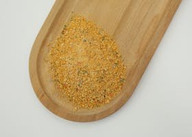 A pile of vibrant seasoning blend rests on a wooden board, showcasing its texture and colors.