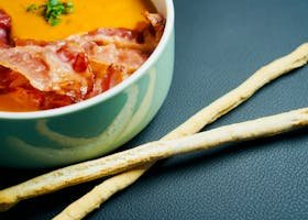 Delicious creamy soup topped with crispy bacon, accompanied by crunchy breadsticks.
