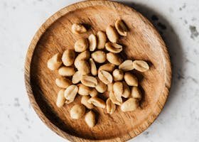 Overhead shot of peeled peanuts served on a rustic wooden plate against a marble background.